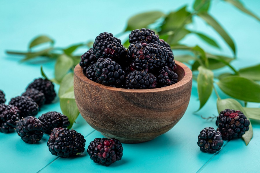 front-view-of-blackberry-in-a-wooden-bowl-on-a-light-blue-surface.jpg