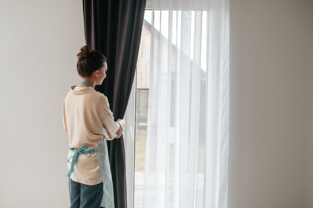 young-woman-standing-near-the-widnow-and-fixing-the-curtains.jpg